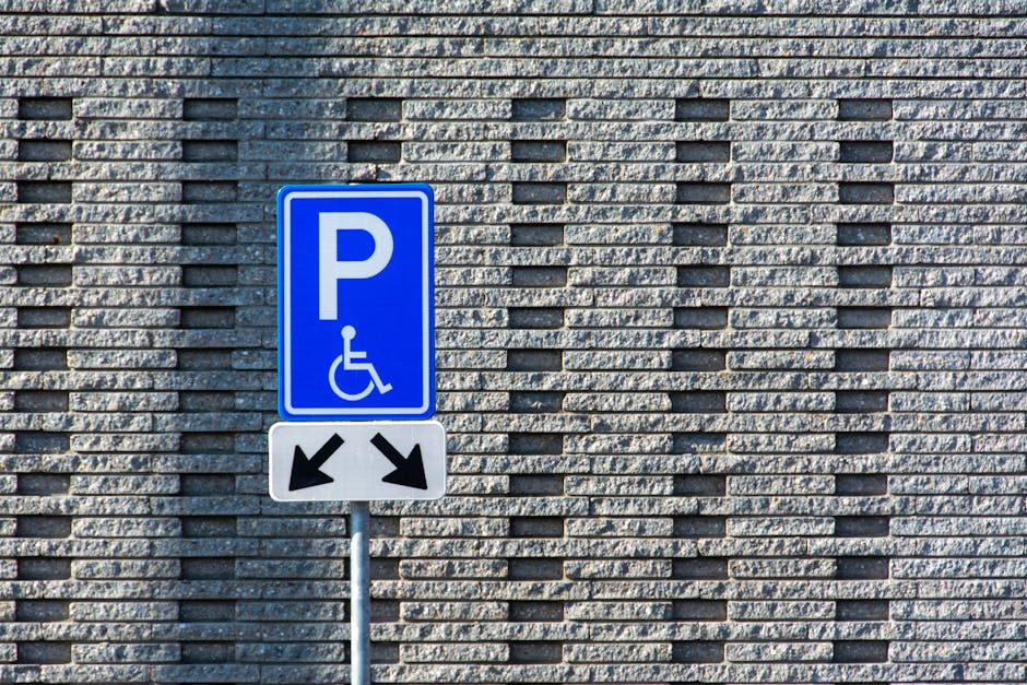 Close-up view of a parking space designated for disabled individuals, with faded yellow lines and a worn wheelchair symbol painted on dark asphalt. The surface of the parking area shows signs of wear,